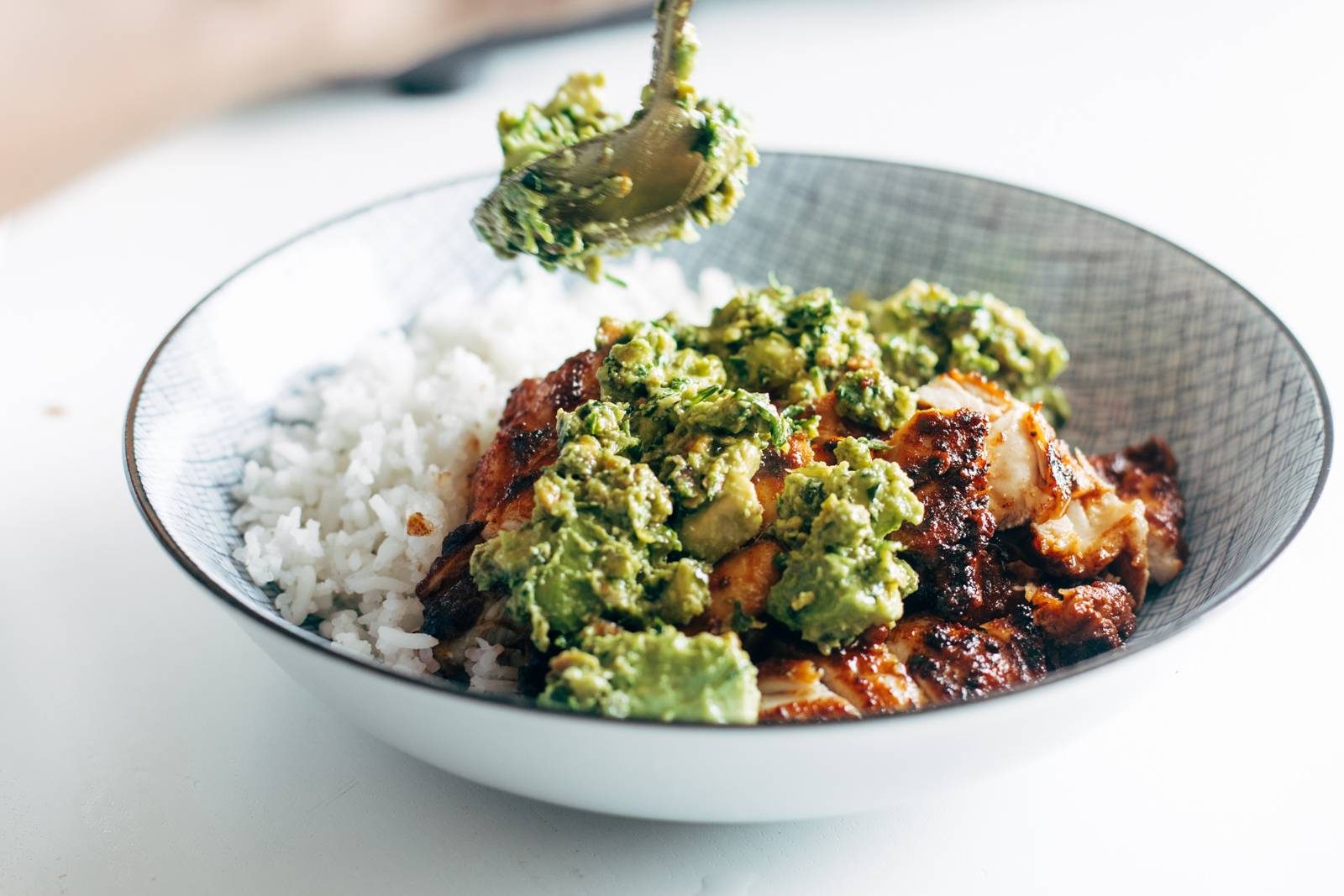 Spooning sauce over chicken and rice in a bowl.