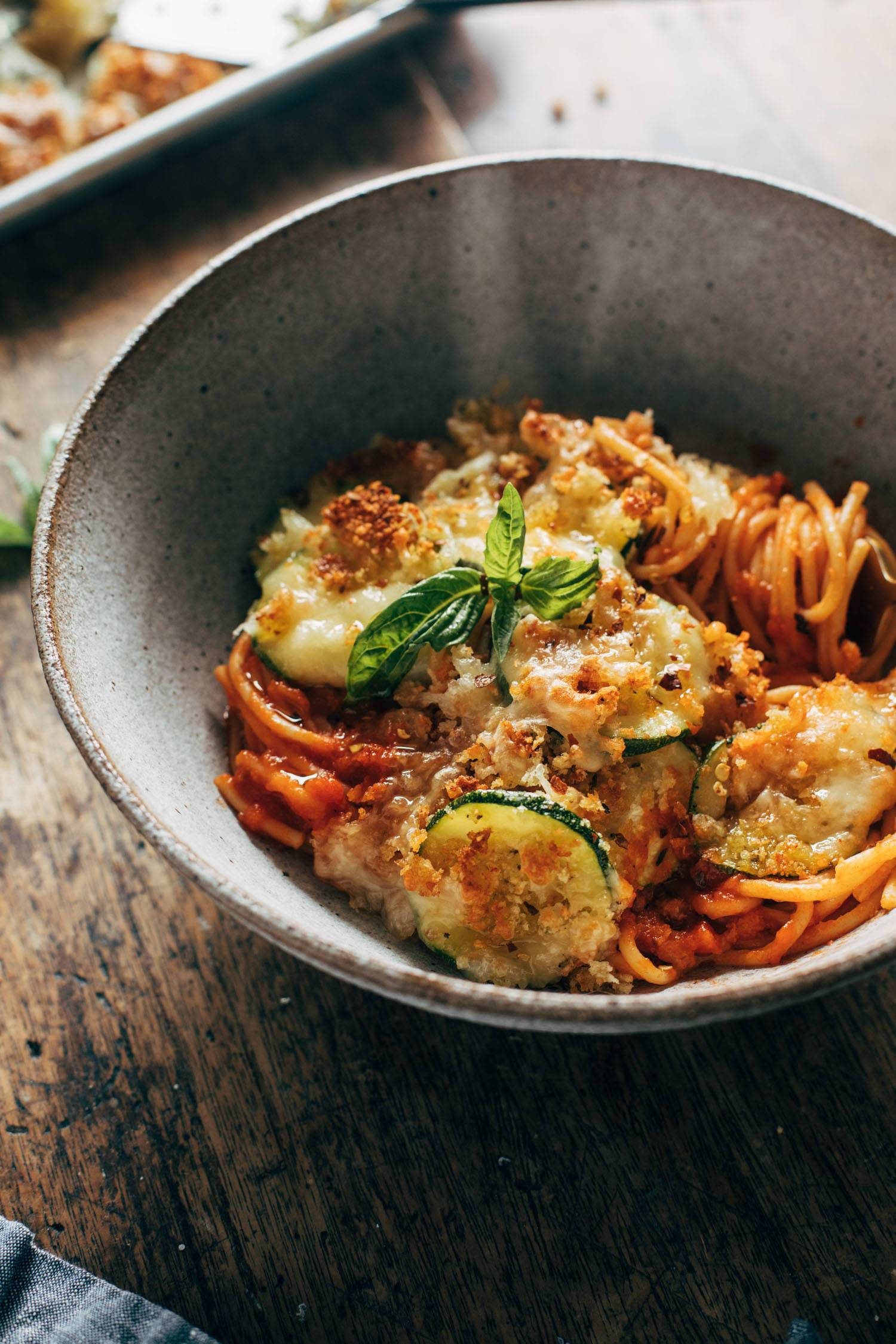 Spaghetti with crispy zucchini in a bowl with melted cheese and fresh basil on top.