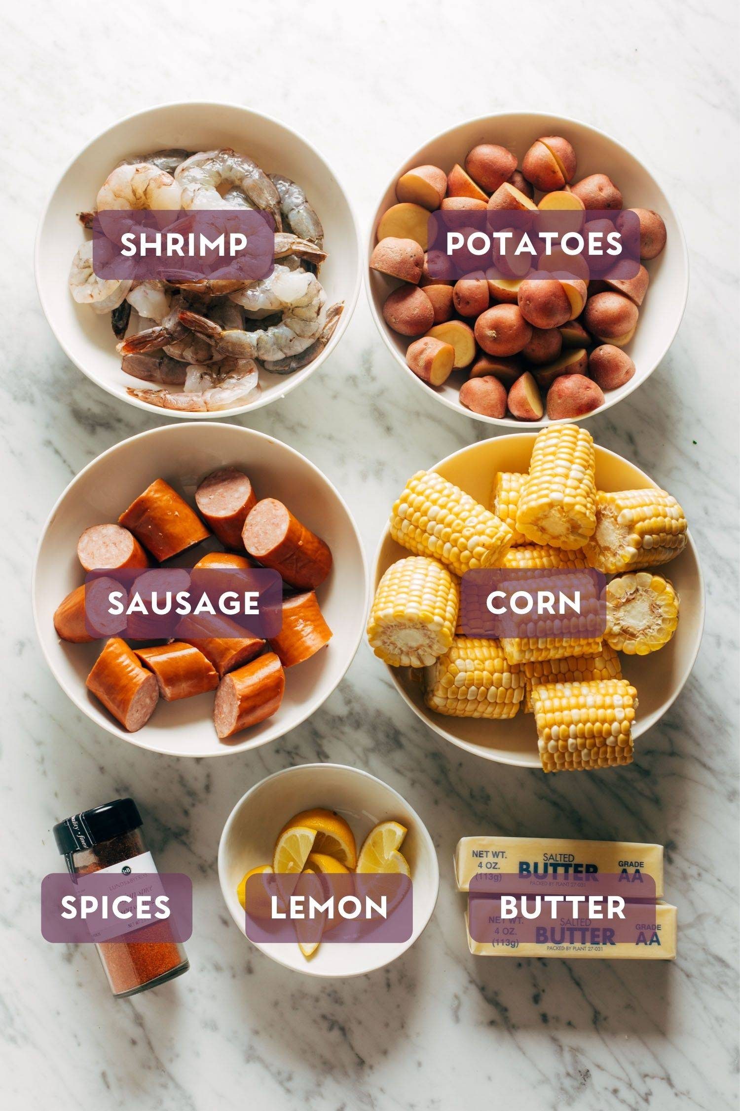 Ingredients for a shrimp boil laid out on a table. There is a purple bubble over each ingredient with the ingredient name in the purple bubble.