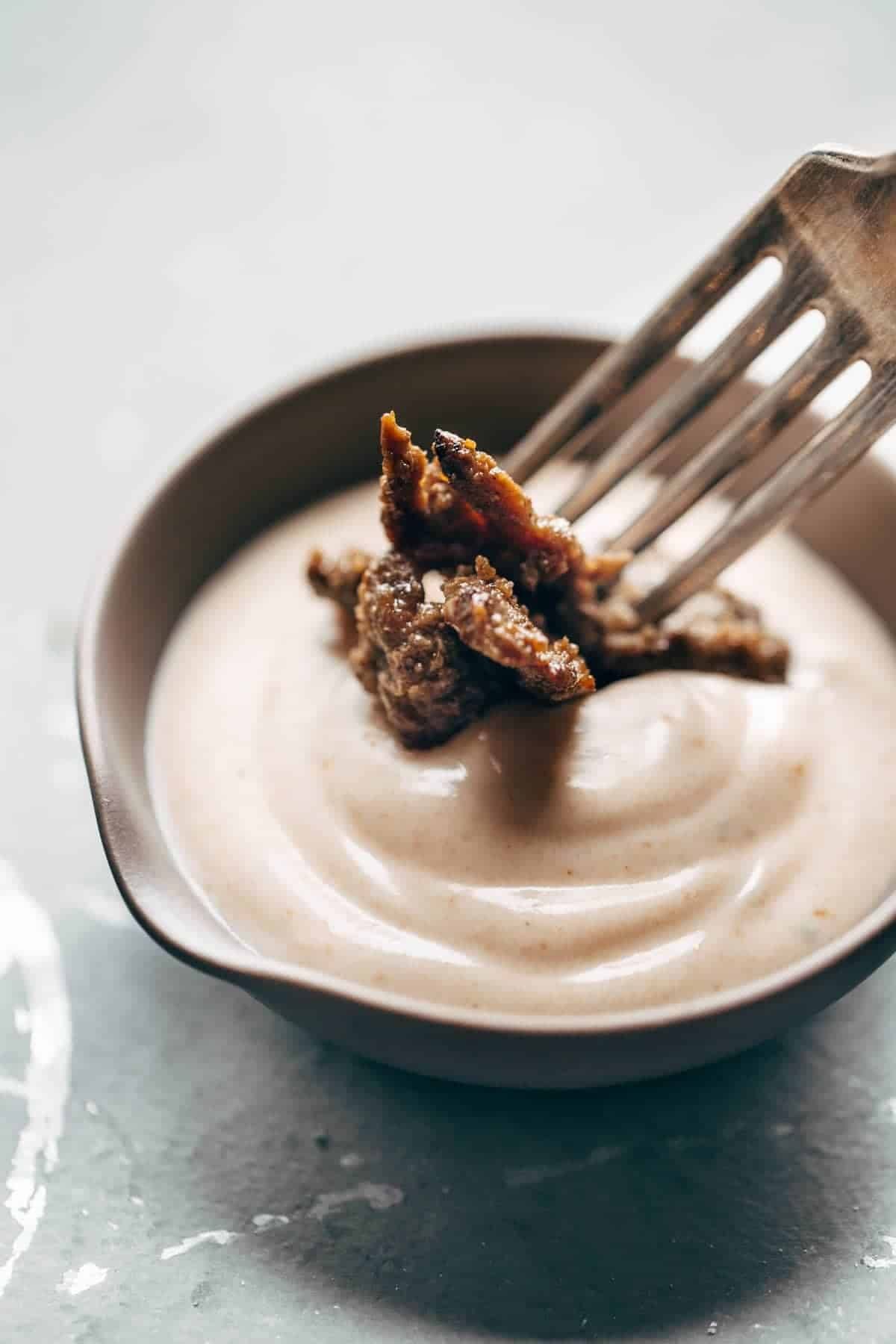 Meat being dipped in yum yum sauce in a bowl.