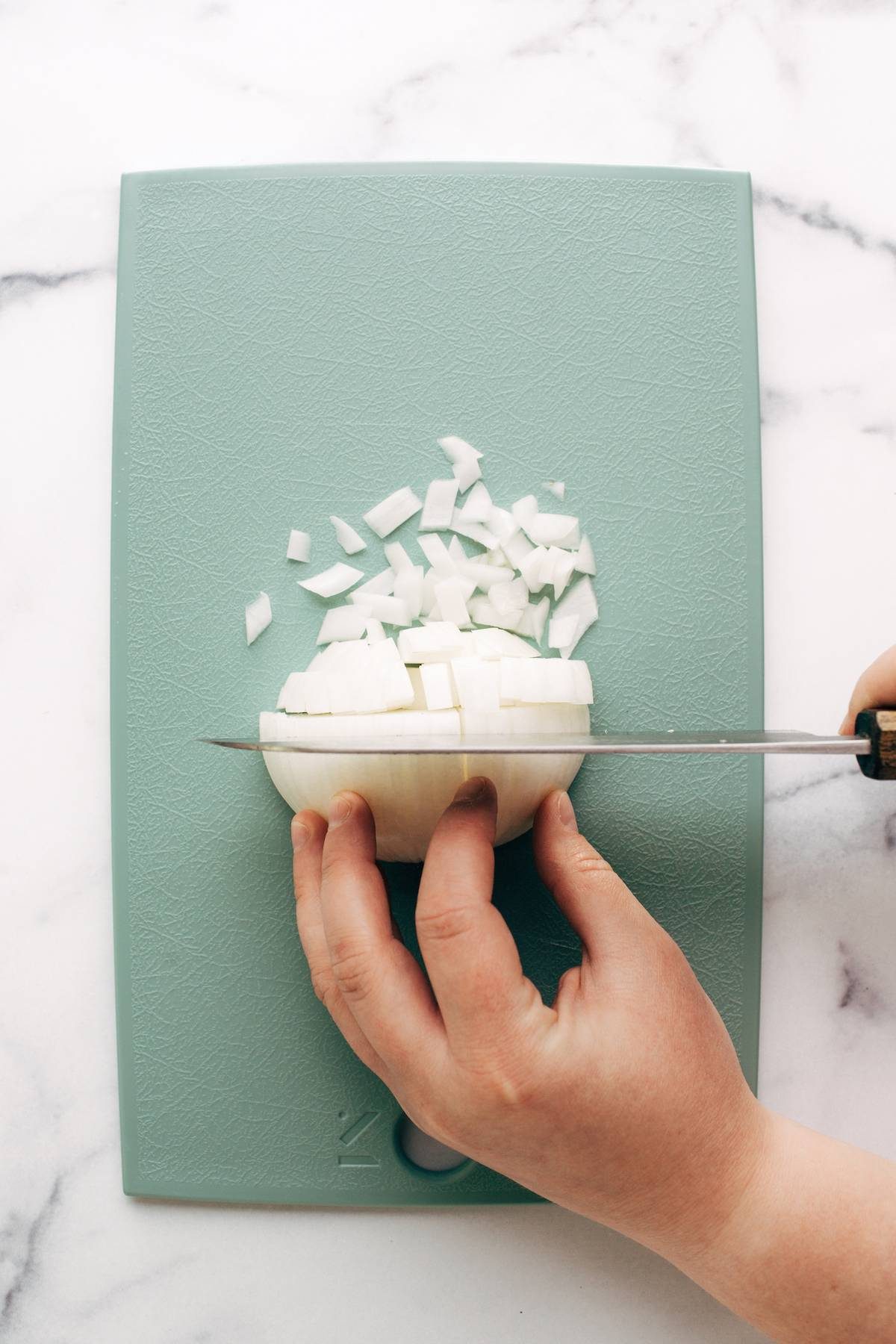 Someone dicing an onion on a cutting board.